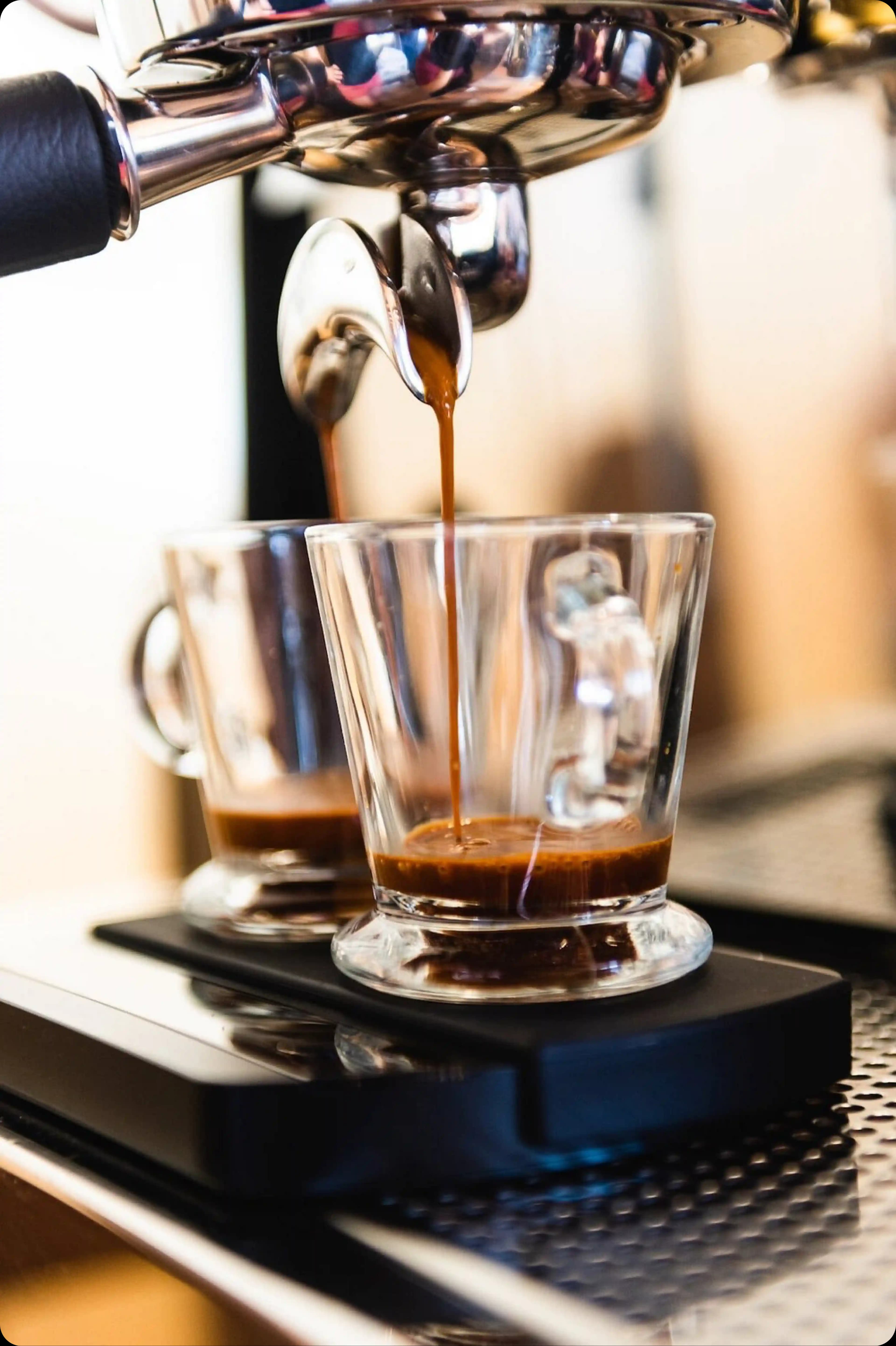 A close-up of a professional espresso machine pouring a rich, dark shot of coffee into two glass cups.