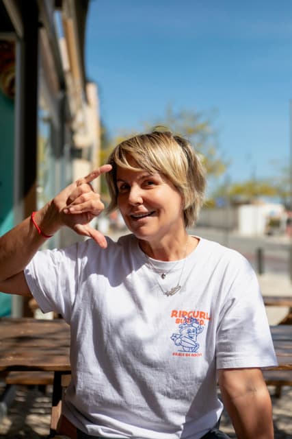 Smiling woman who ist part of the staff making a surf hand gesture outdoors on a sunny day.