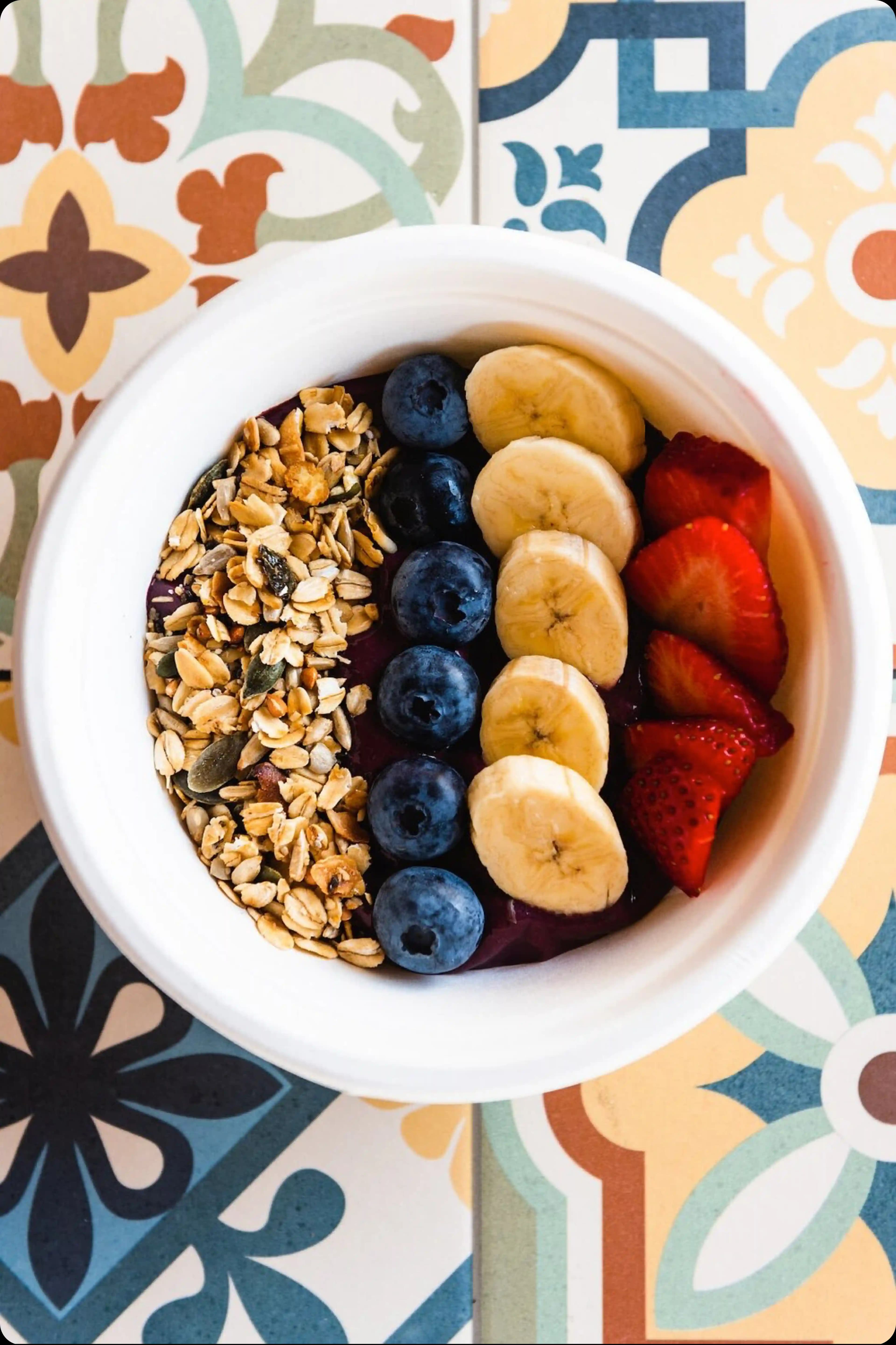 An açaí bowl topped with granola and fresh fruit, including banana, strawberries, and blueberries.