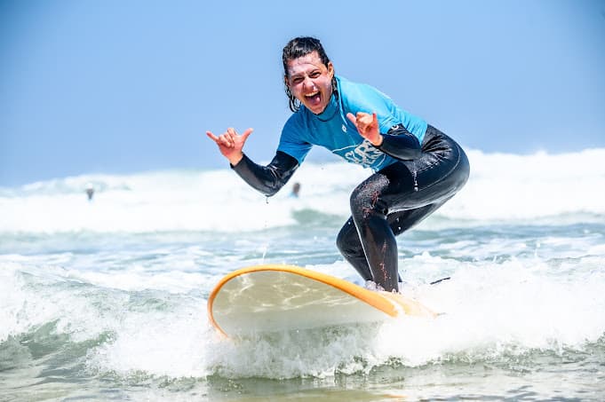Excited surfer riding a wave and making a shaka hand sign.