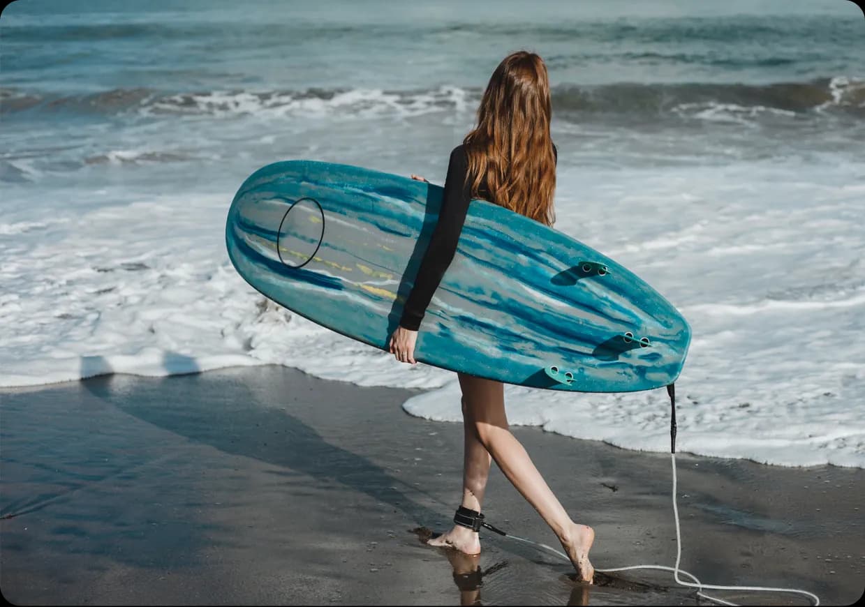 A woman carrying a softboard under her arm on the beach