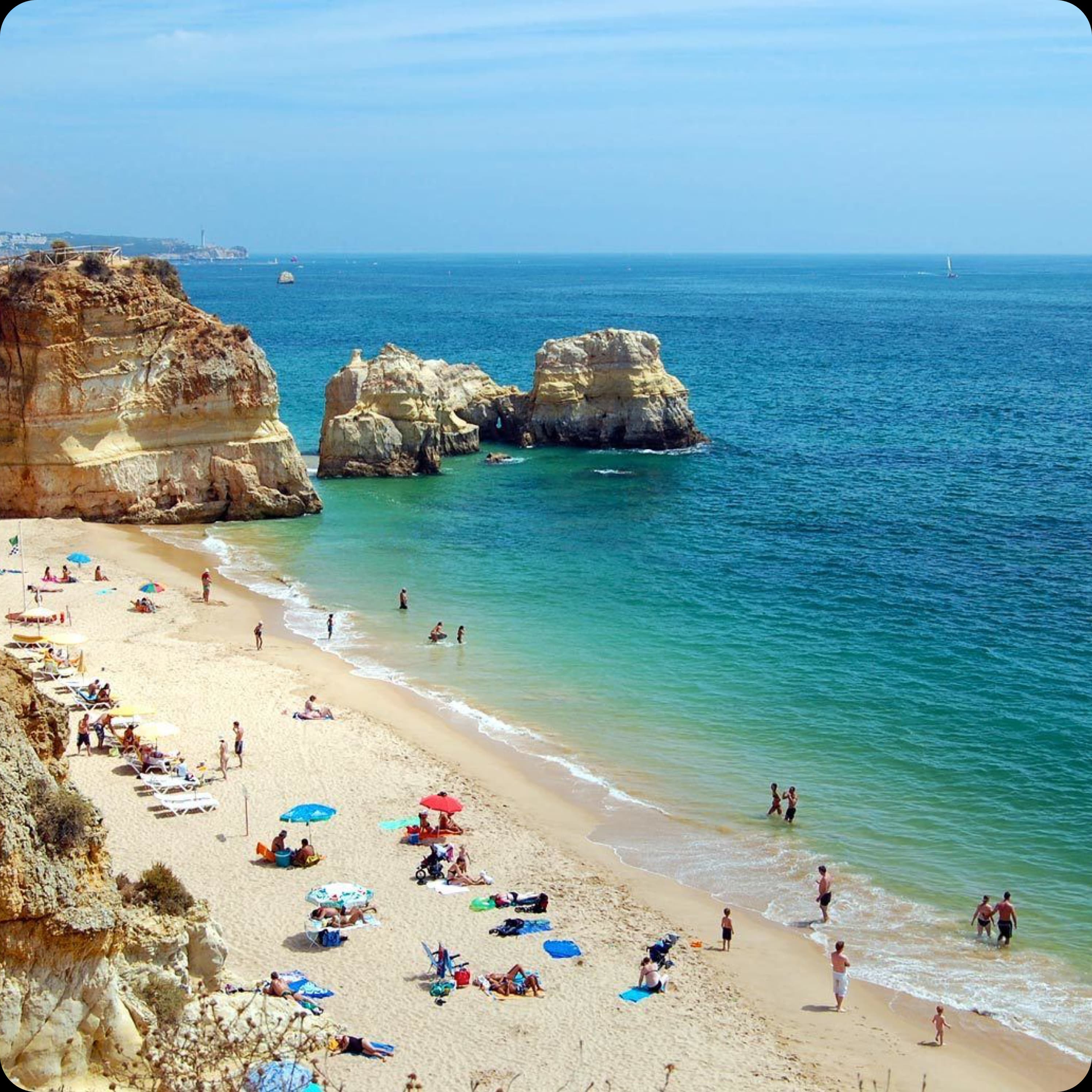 A sunny day at a picturesque Algarve beach, with people relaxing on the sand and swimming in the blue ocean.