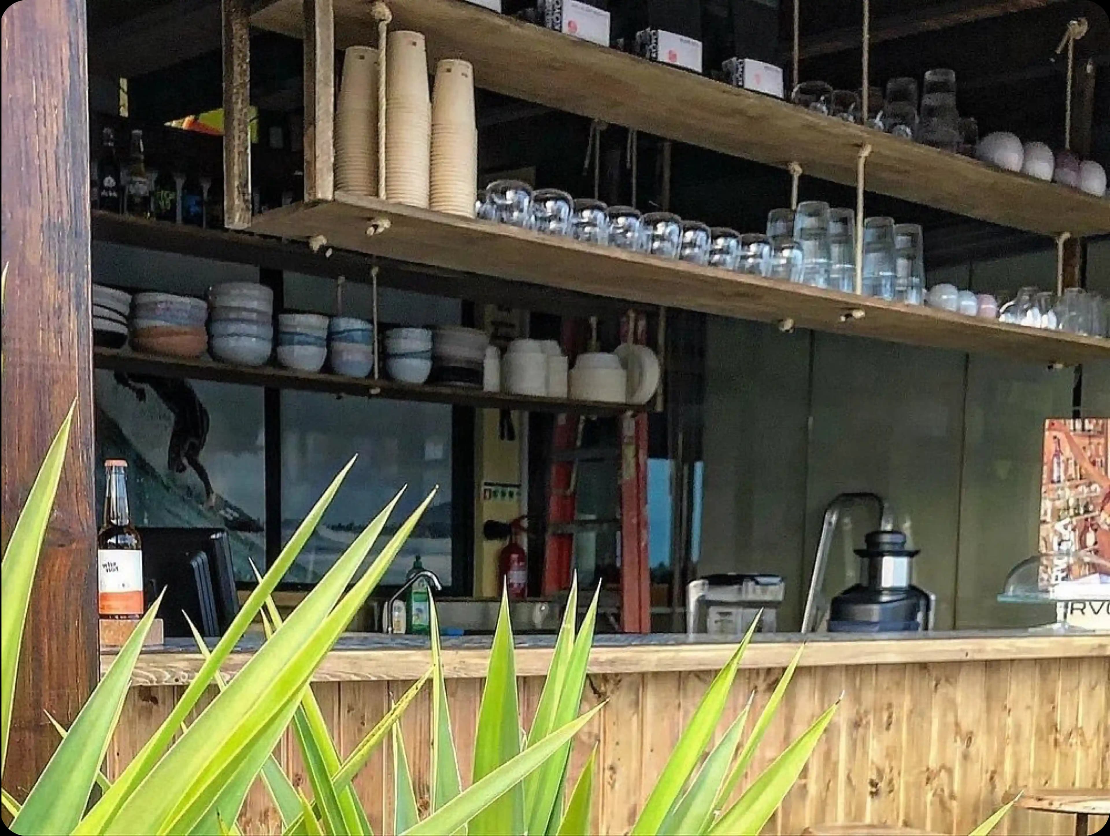he well-stocked bar area of the cafe, with shelves of cups and glasses, seen from an outdoor perspective.