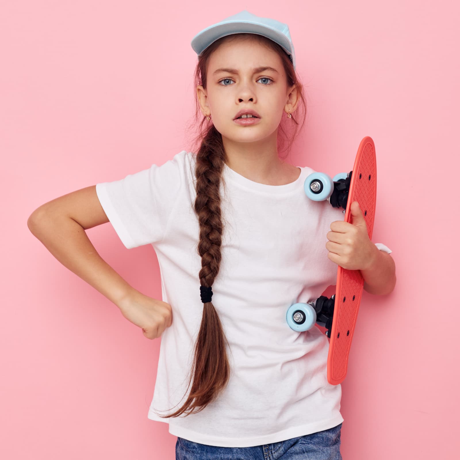Stylish young woman in a light blue cap holding a skateboard against a solid pink background.